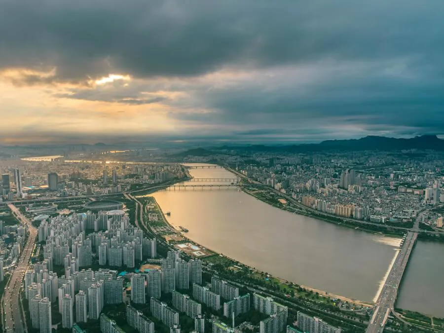 The Han River at dusk seen from high above Jamsil, with bridges, apartment towers and hills on the horizon